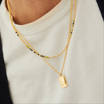 Gold necklace with a pendant on a person wearing a white shirt.